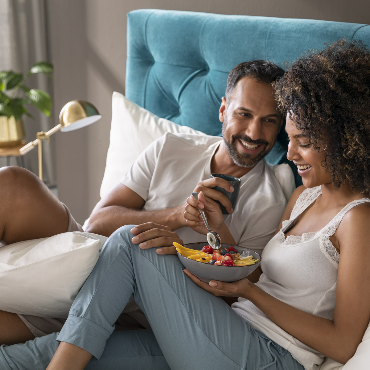 Mistral Boxspringbett Paar essen Frau mit Fruchtbowl Mann mit Tasse auf Boxspringbett liegend